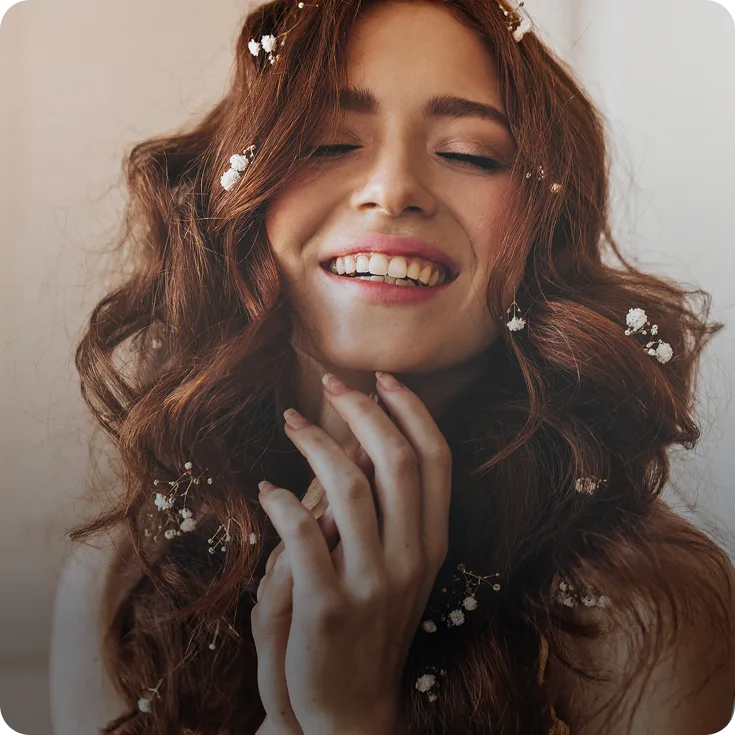 Woman with long brown hair smiling with eyes closed, touching her neck